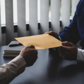 A man hands a file to another man, implying the exchange of an appointment letter for a placement.